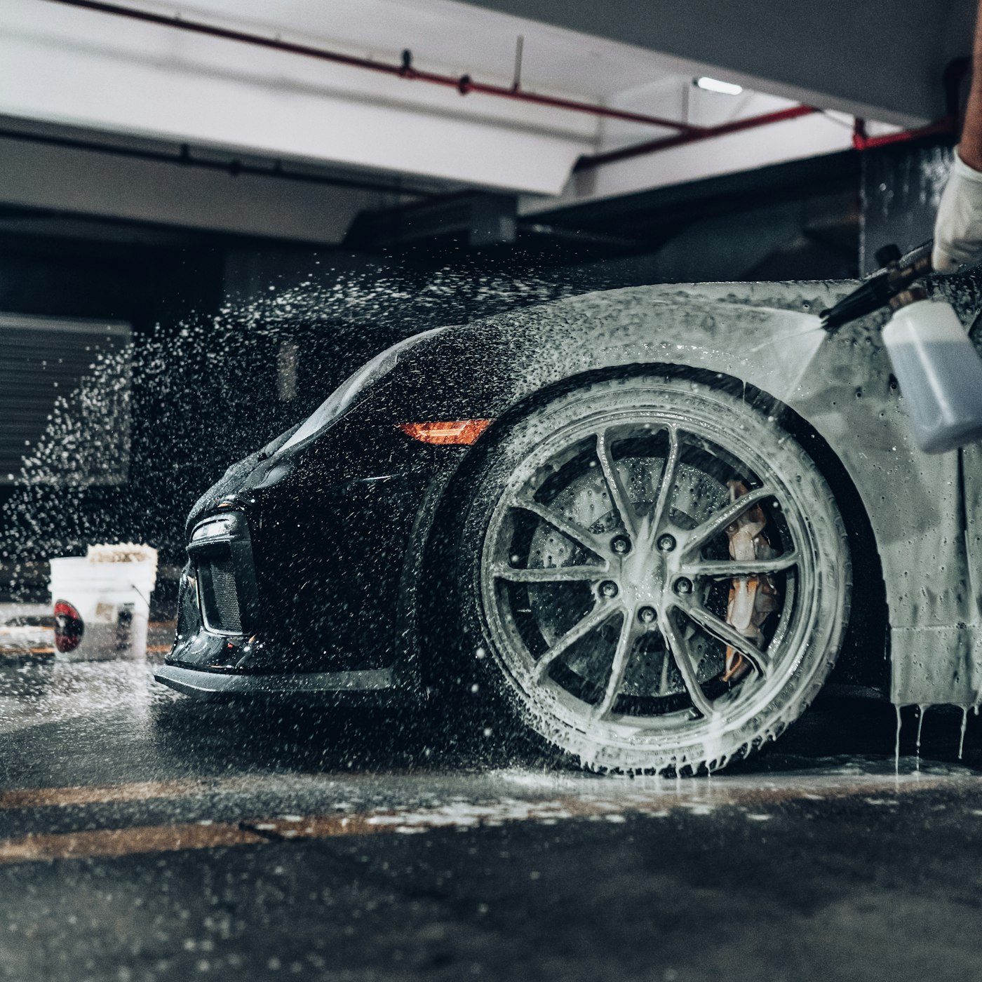 Detailer covering a black sports car in snow foam inside the studio