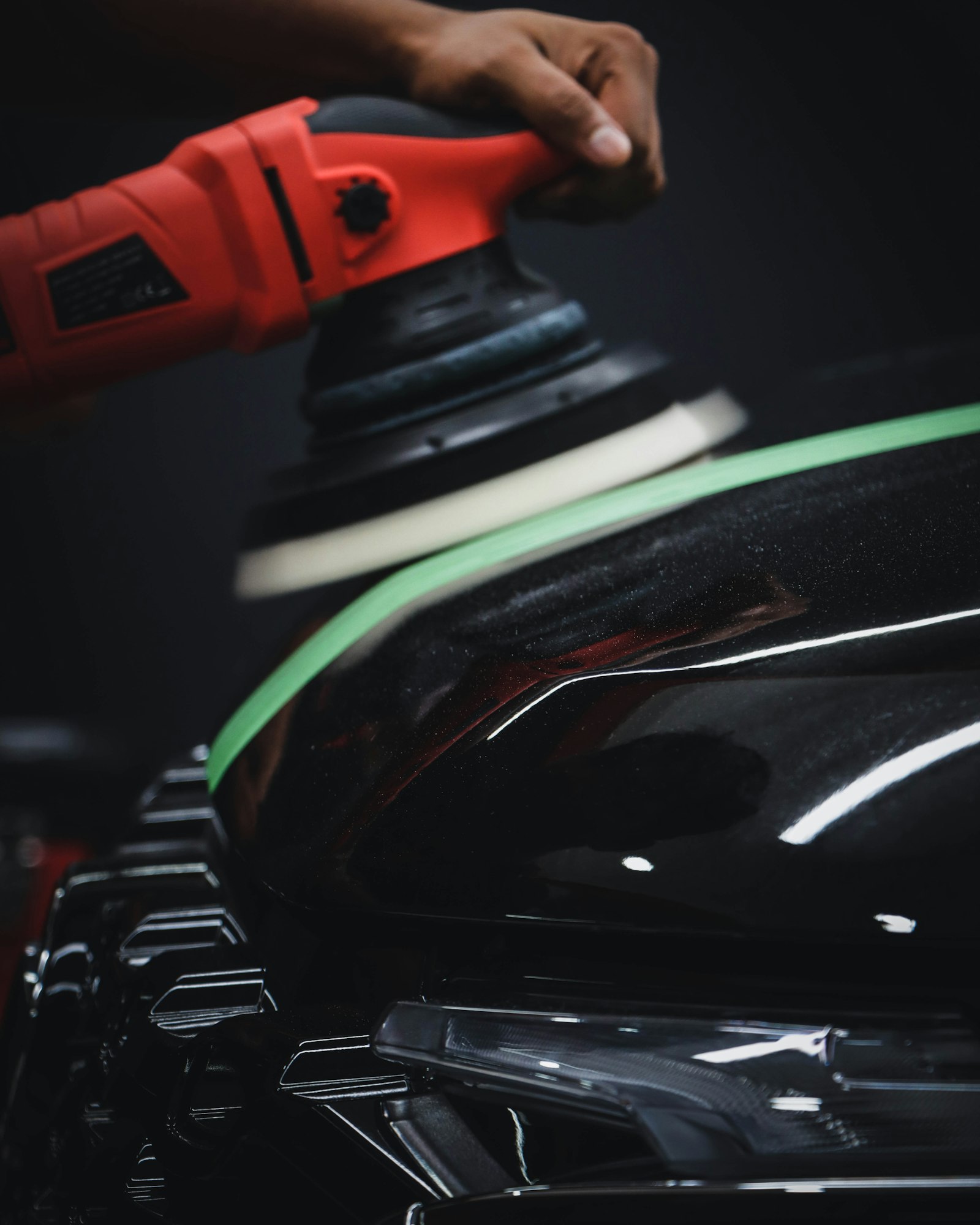Red and black machine polisher resting on a car panel